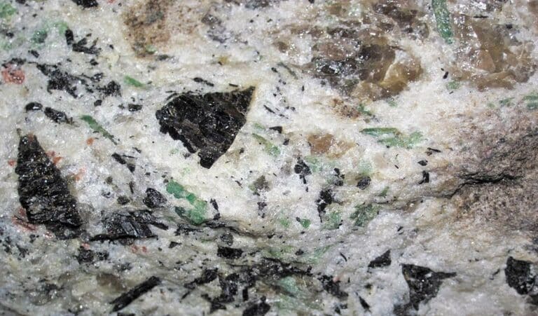 Crabtree Pegmatite from Devonian of North Carolina, USA. It has schorl tourmaline (black), Emeralds (green), and garnet (pinkish-reddish) in (grayish) and quartz (medium-brown glassy)crystals